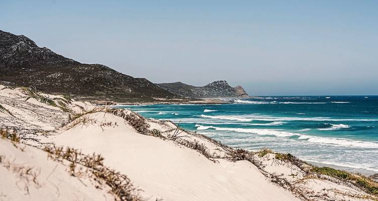 Sandy beach with distant mountains under a clear blue sky.