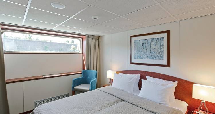 Cabine de navire de croisière avec un lit et des œuvres d'art au-dessus de la tête de lit.