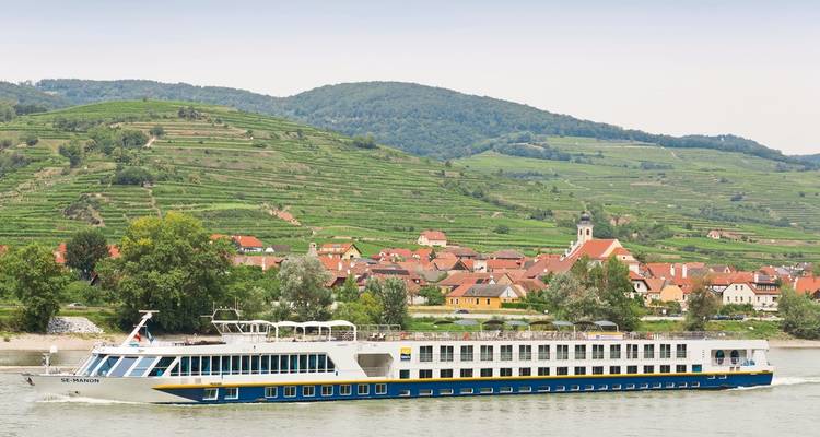 Bateau de croisière sur une rivière avec des villages pittoresques et des vignobles.
