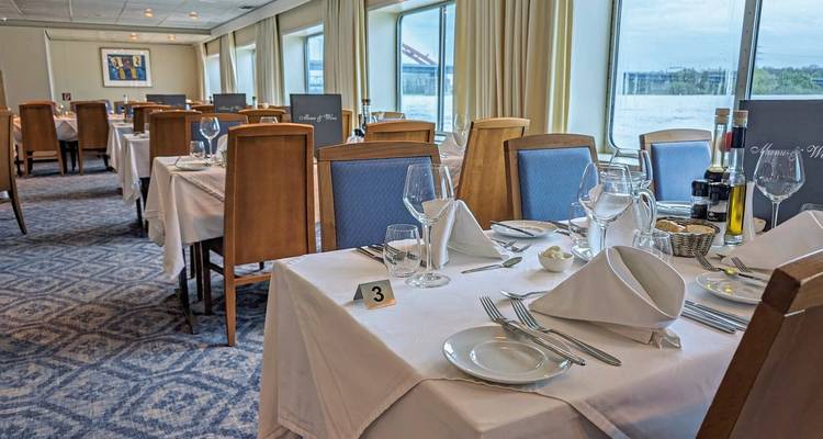 Salle à manger sur un bateau de croisière fluviale avec des tables dressées pour les repas.