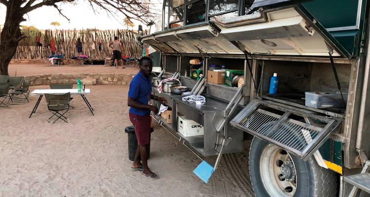 Man standing at an outdoor kitchen setup with tents in the background.