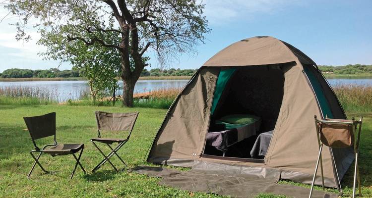 Tent and chairs by a lakeside under a tree.