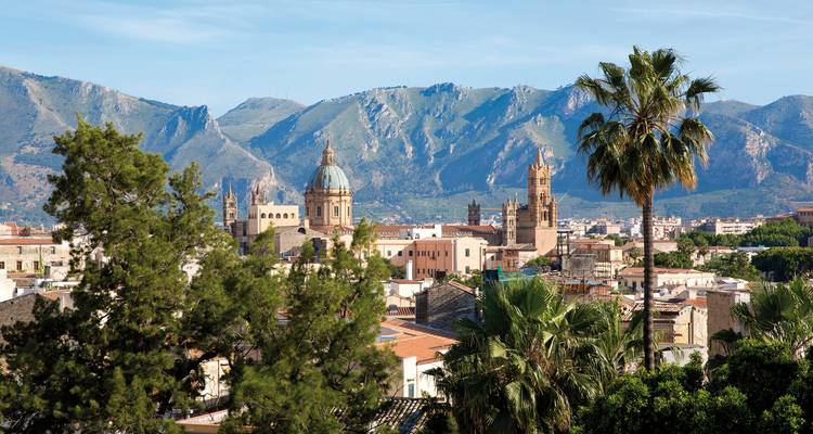 Stadsgezicht met bergen op de achtergrond, met groene ruimtes.