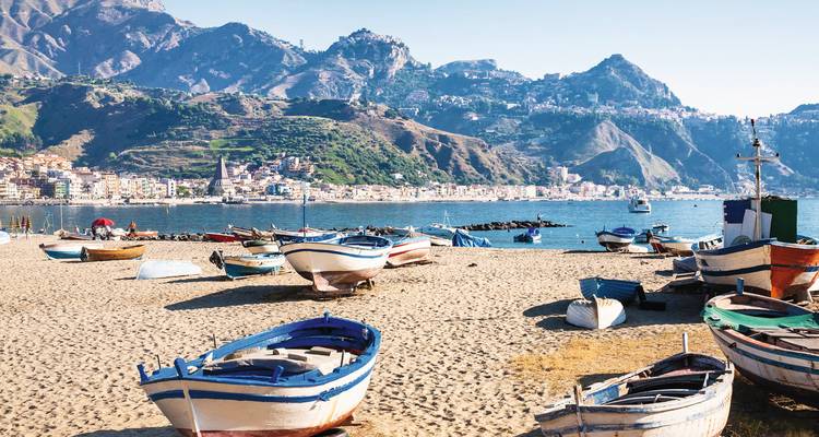 Strand met boten en bergachtige achtergrond.