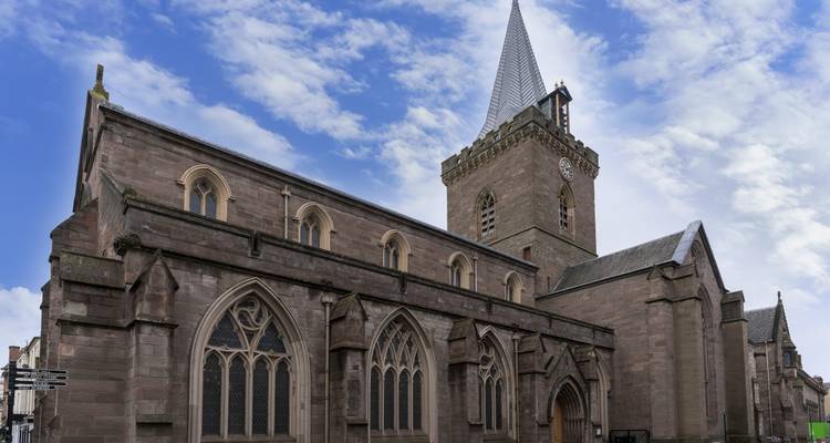 Een oude stenen kerk met een hoge toren tegen een gedeeltelijk bewolkte hemel.