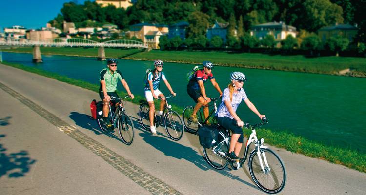 A group of cyclists riding by a river with a scenic backdrop.