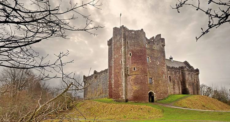 Le château de Doune se dresse majestueusement au milieu d'arbres dénudés et d'un ciel nuageux.