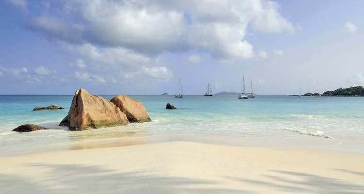 Plage tranquille avec des voiliers à l'horizon.