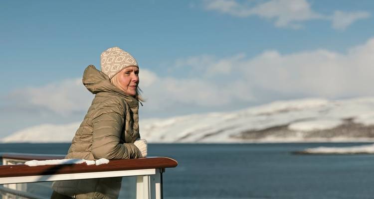 Femme sur le pont d'un navire, portant un manteau d'hiver et un chapeau, regardant la mer.