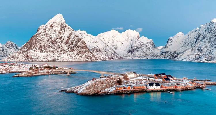 Village norvégien enneigé au bord de la mer avec un arrière-plan montagneux.