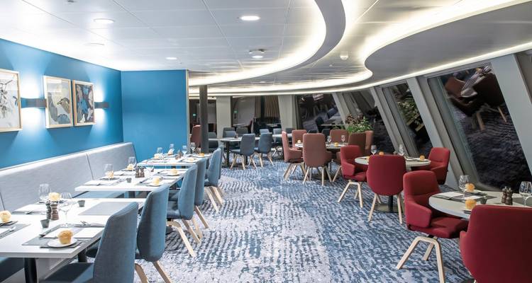 Une salle à manger moderne avec des chaises bleues et rouges et des tables dressées sur un navire.