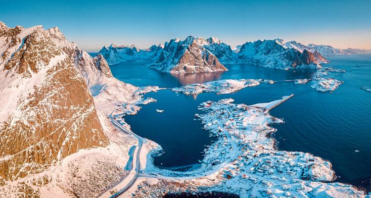 Vue aérienne de montagnes enneigées et d'un fjord sous un ciel dégagé.