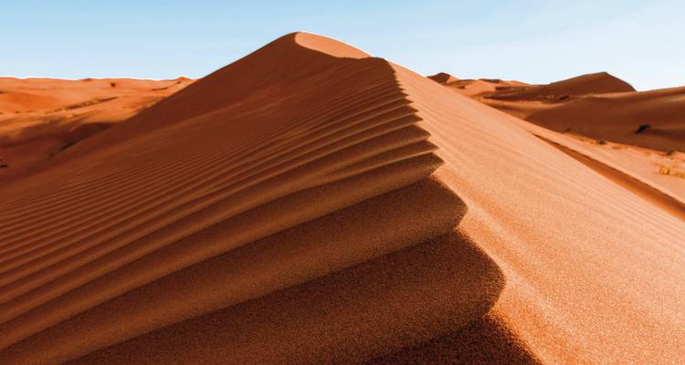 Rote Sanddüne mit scharfen Graten in einer Wüste.