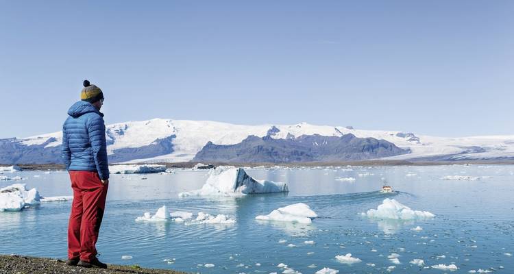 Personne en vêtements d'hiver observant des icebergs dans un lagon glaciaire.