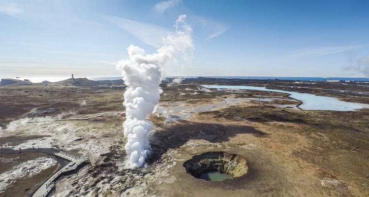 Geyser actif en éruption dans un paysage accidenté.