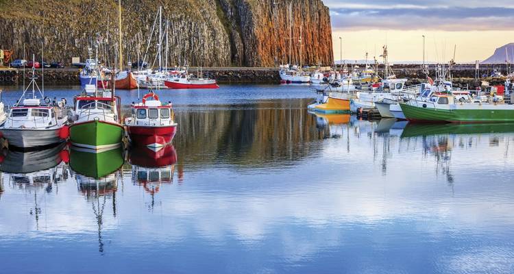 Ein Hafen voller bunter Fischerboote mit hohen Klippen im Hintergrund.