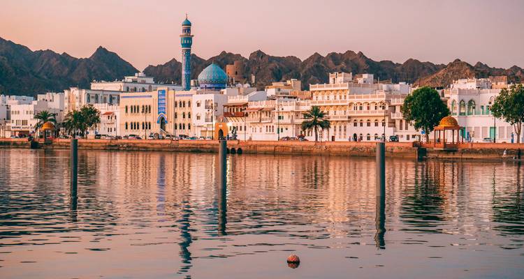 Stadtansicht mit weißen Gebäuden und Moschee am Wasser bei Abenddämmerung.