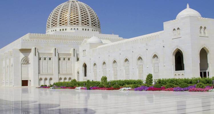 Weiße Moschee mit goldener Kuppel und lebendigen Gärten.