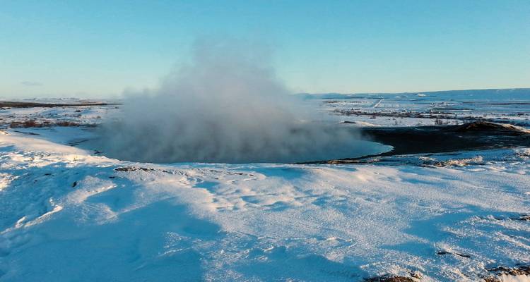 Geysir bricht inmitten einer verschneiten isländischen Landschaft aus.