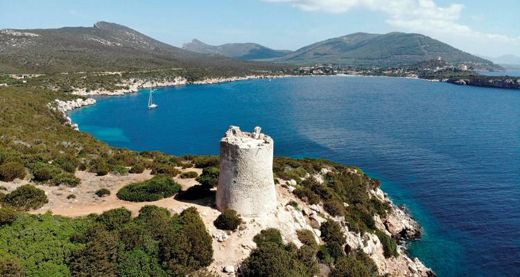 Old stone tower overlooking a coastal bay with a sailing boat.