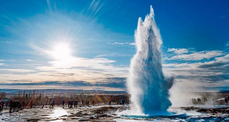 Ein Geysir, der gegen einen strahlend sonnigen Himmel ausbricht.