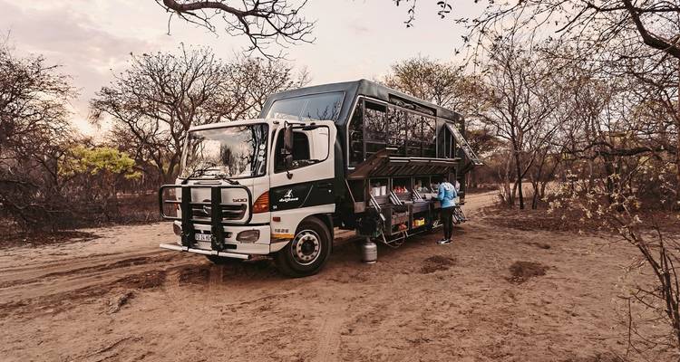 Camión de expedición equipado para safari estacionado en un área seca y boscosa.