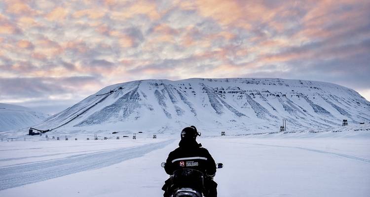 Personne conduisant une motoneige à travers une plaine enneigée avec des montagnes.