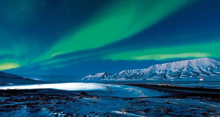 Aurore boréale au-dessus d'un paysage enneigé la nuit.