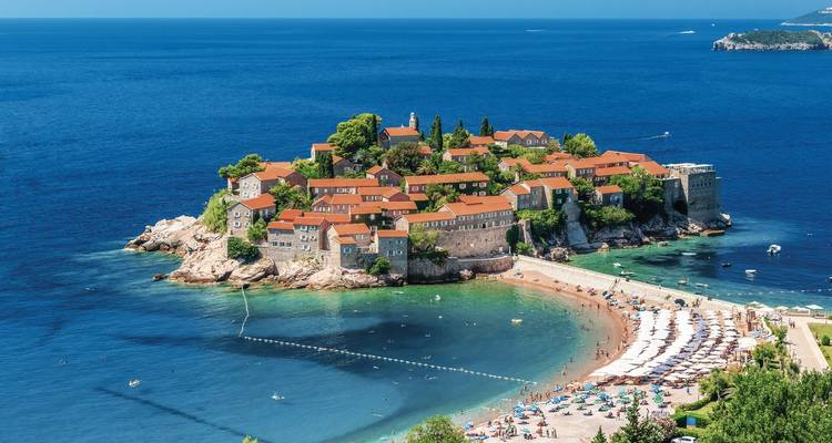 Île avec des bâtiments historiques et une plage, entourée par la mer bleue.