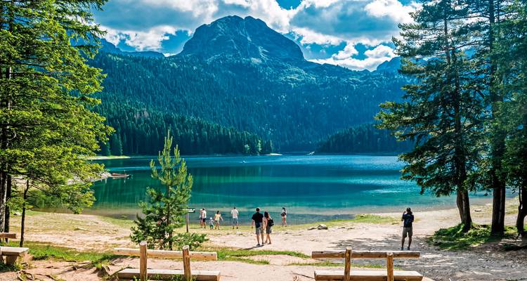 Menschen genießen einen klaren See, umgeben von üppigem Grün und Bergen.