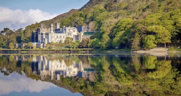 Ein Schloss, das sich in einem stillen See spiegelt, umgeben von Bäumen.