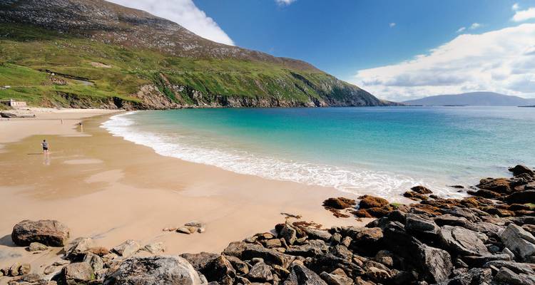 Sandiger Strand mit türkisfarbenem Wasser und felsiger Küstenlinie.