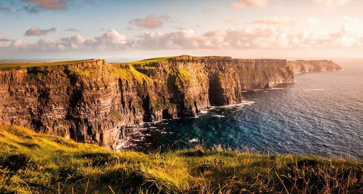 Vue panoramique le long des falaises escarpées de Moher avec une lumière dorée du soir.
