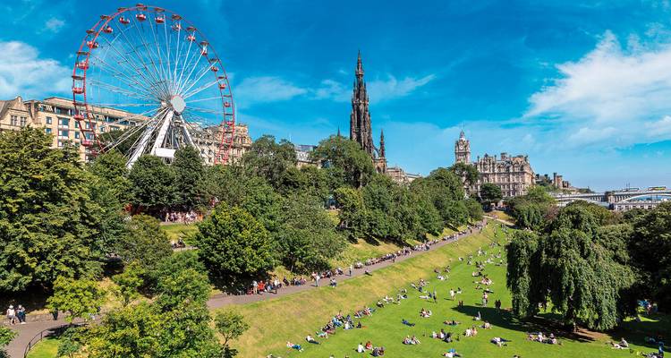 Park in Edinburgh with a ferris wheel and historic buildings.