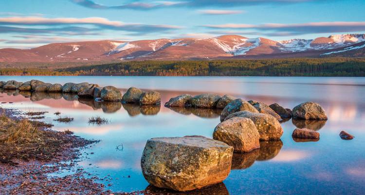 Serene lake with rocks and mountains reflecting in the water.