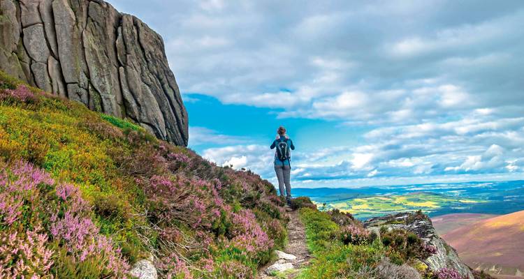 Person hiking on a path with rocky outcrops and distant views.