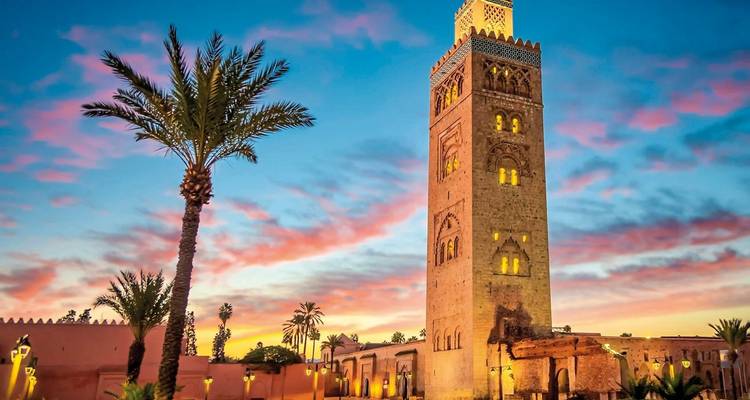 Der Koutoubia-Moschee-Turm ragt gegen einen leuchtenden rosa und blauen Sonnenuntergangshimmel mit Palmensilhouetten empor
