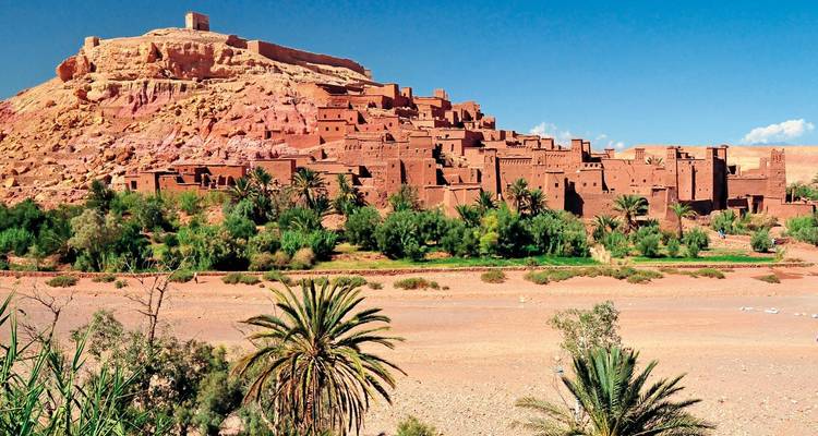 Lehmksar von Ait Benhaddou auf einem Hügel über einer üppigen Oase unter klarem Himmel thronend