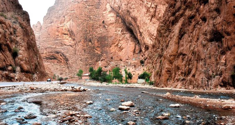 Steile rote Canyonwände der Todra-Schlucht mit einem seichten steinigen Fluss, der durch den Talboden fließt