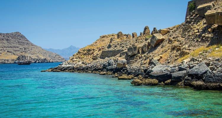 Rotsachtige kustlijn met helder blauw water en heuvelachtige achtergrond.