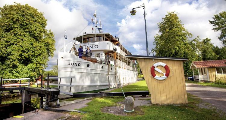 A boat named Juno docked near a small wooden building.