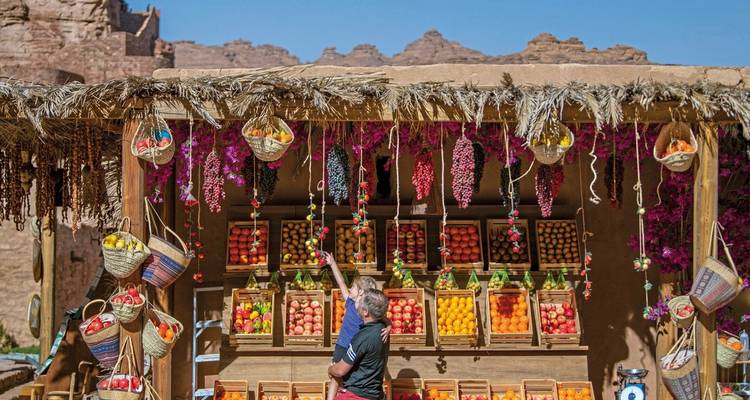 Local market stall with colorful produce and people shopping.
