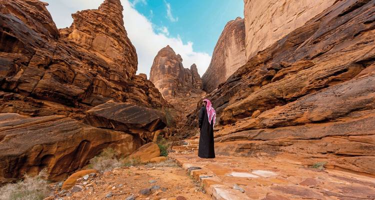Person walking through a canyon with towering rock formations.