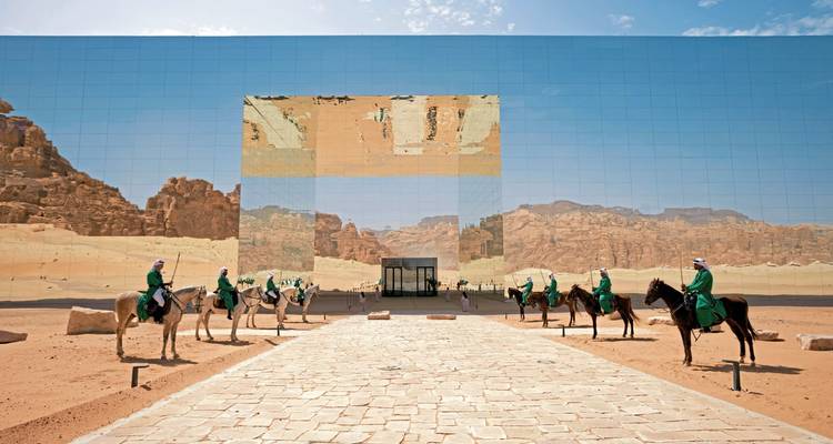 Line of people on horses in front of a mirrored building in the desert.