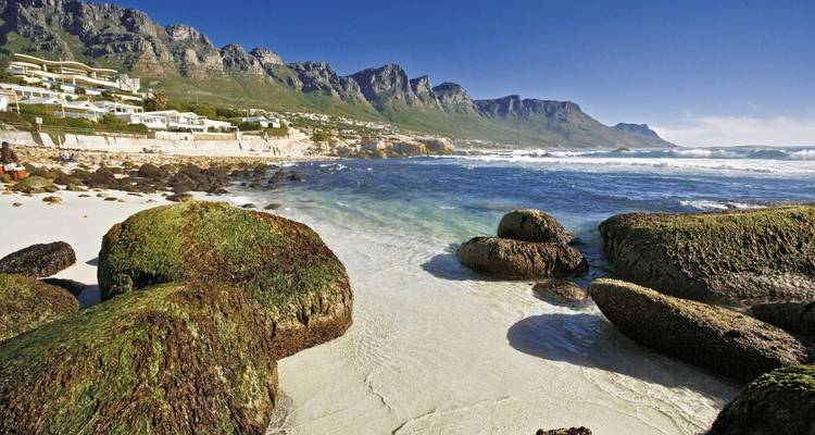 Rotsen op een zandig strand met bergen op de achtergrond.