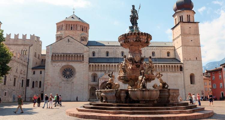 Place avec une fontaine historique et une église, entourée de gens.