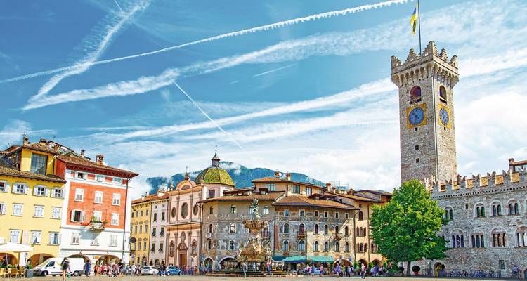 Historischer Glockenturm und farbenfrohe Gebaeude, die einen lebhaften italienischen Platz unter streifig blauen Himmelszuegen umgeben.