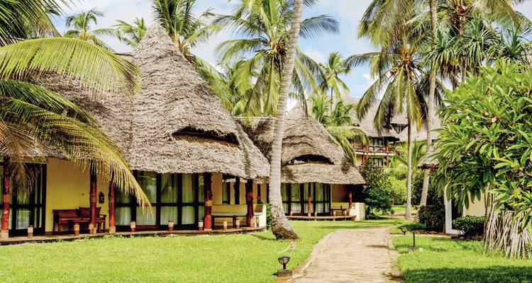 Cottages rustiques au toit de chaume dans un cadre de jardin tropical verdoyant.