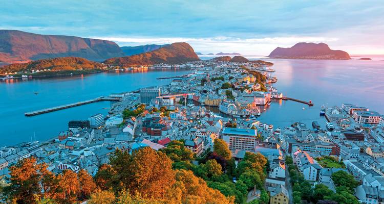 Panorama aéreo de gran altura de la península de Ålesund rodeada de fiordos azul profundo a la luz del amanecer.