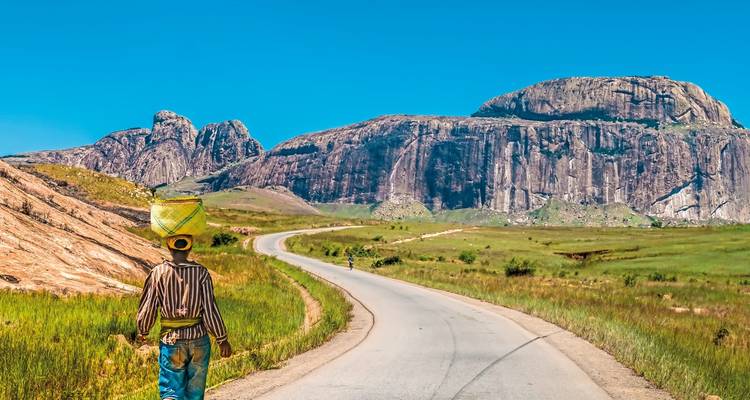 Person, die entlang einer Straße mit felsigen Hügeln geht.